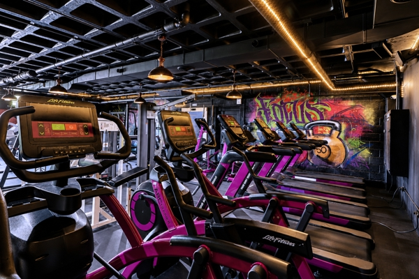 Row of treadmills, ellipticals and bikes beside a graffiti mural at BodyByFlo