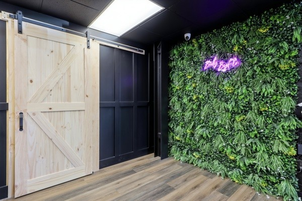 Living green wall with the BodyByFlo neon sign beside a sliding barn door