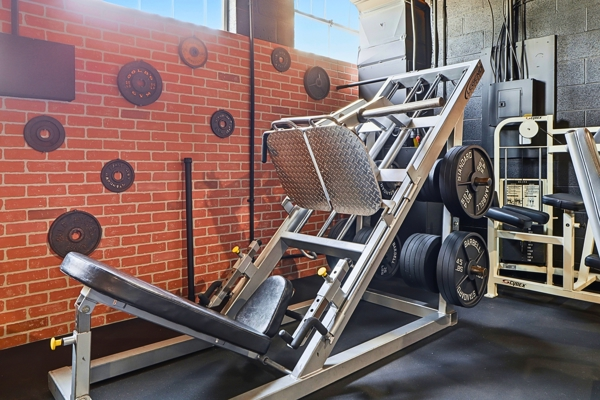 Plate-loaded leg press machine beside a brick wall hung with weight plates