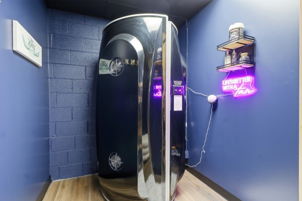 Automated spray tan booth beside a Life is Better with a Tan neon sign