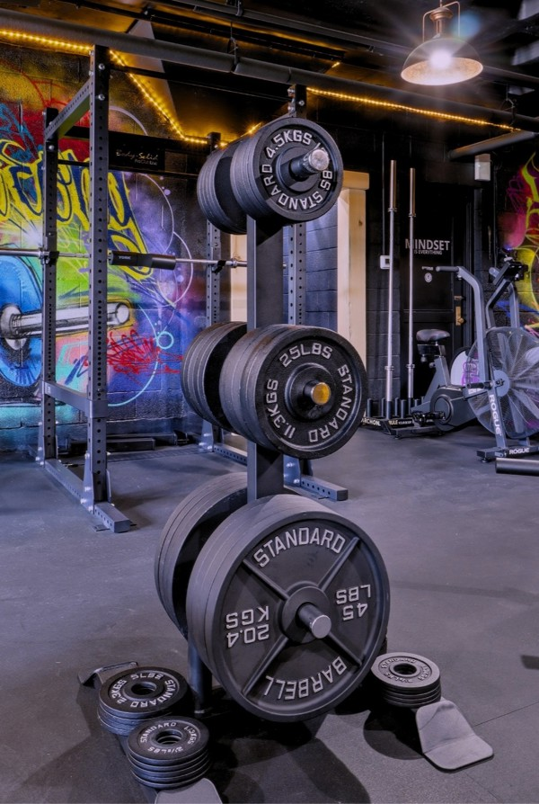 Loaded plate tree beside a power rack in front of a colourful graffiti mural